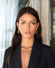Load image into Gallery viewer, An elegant woman dressed in a black suit, complemented by gold jewelry, notably a striking chunky cuban chain necklace.