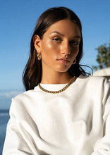 Load image into Gallery viewer, A woman showcases her fashion-forward style by pairing a white sweater with a striking gold chain necklace, making a bold statement.