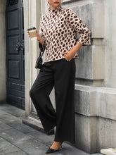 Load image into Gallery viewer, Person wearing a leopard print top and black pants, standing against a stone wall.