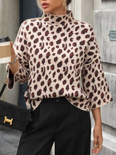 Load image into Gallery viewer, Person wearing a leopard print top and holding a coffee cup, standing against an urban background.