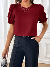 Load image into Gallery viewer, Person wearing a red blouse with puff sleeves and navy pants in an indoor setting.