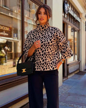 Load image into Gallery viewer, Woman wearing a leopard print top and black pants, holding a black handbag, standing on a street.