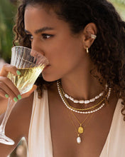 Load image into Gallery viewer, A woman clad in a white dress and adorned with pearls indulges in a sip from her glass. She showcases an exquisite half pearl half chain necklace, striking the perfect balance between trendy and timeless.
