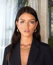 Load image into Gallery viewer, An elegant woman dressed in a black suit, complemented by gold jewelry, notably a striking chunky cuban chain necklace.
