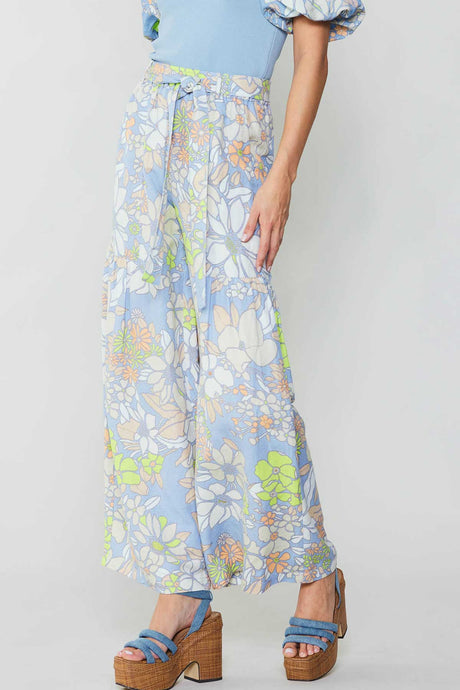 The model looks stylish in a blue top and wide-leg floral print pants, cinched at the waist with a self-tie belt.