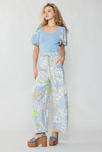 Load image into Gallery viewer, A fashionable model dons a blue top and wide-leg floral print pants, creating a chic and comfortable ensemble.
