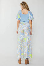 Load image into Gallery viewer, Elegantly attired, the model exudes grace and style with a stunning blue top and wide-leg pants adorned with a retro-inspired floral pattern.
