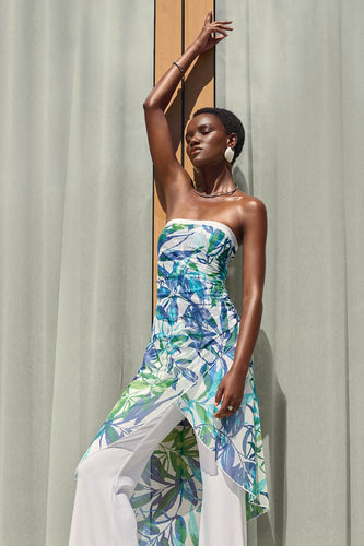 Silky knit strapless jumpsuit in blue and green, worn by a woman posing gracefully. Vibrant tropical print adds irresistible appeal.