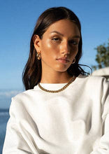 Load image into Gallery viewer, A woman showcases her fashion-forward style by pairing a white sweater with a striking gold chain necklace, making a bold statement.
