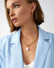 Load image into Gallery viewer, A woman wearing a blue blazer and gold chain necklace. The necklace features a natural pearl on a chunky gold chain with a T bar closure. Elevate your outfit with this trendy and unique accessory.
