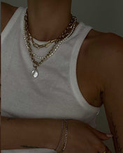 Load image into Gallery viewer, A woman in a white tank top adorns a timeless pearl necklace. The necklace boasts natural freshwater pearls that can be worn in various stylish ways, whether alone or layered with other chains.
