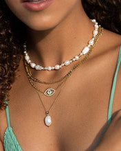 Load image into Gallery viewer, Woman wearing subtle gold eye and pearl pendant necklace. Versatile for layering and styling. 1.5 cm natural baroque pearl on a dainty gold chain. 46 cm length with 8 cm extension chain.
