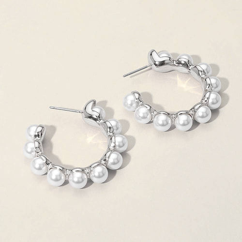 Silver hoop earrings with white pearl beads arranged along the hoop. The earrings have a shiny, metallic finish