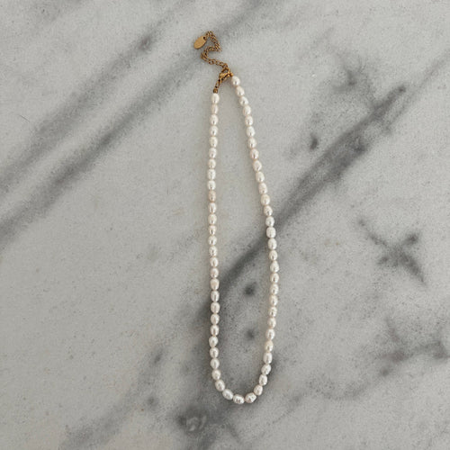 A pearl necklace with an adjustable gold clasp. The pearls are uniformly sized, conveying simplicity and elegance.