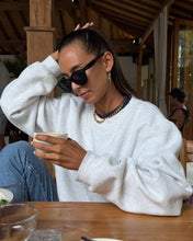 Load image into Gallery viewer, A fashion-forward woman at a table, sporting a white sweatshirt and sunglasses, showcasing a chunky cuban chain necklace.
