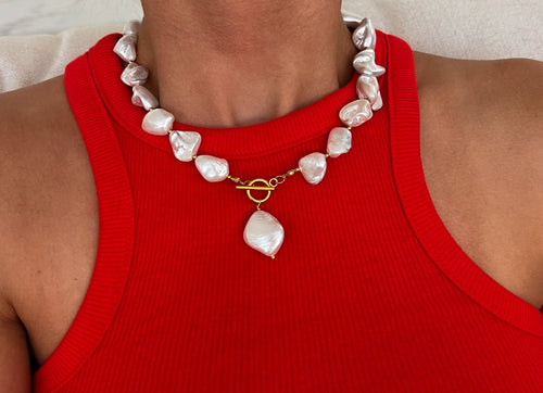A woman wears a chunky white pearl necklace with a gold clasp and pendant, conveying elegance and boldness.