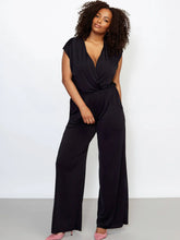 Load image into Gallery viewer, Black stretchy jumpsuit with elastic waist, deep pockets, gathered shoulders, and optional plunging neckline. Wrinkle-free and sleek with laser-cut sleeves and hem.
