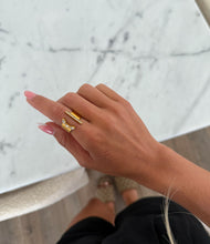 Load image into Gallery viewer, A gold ring with an open design is set against a textured marble surface. The ring features a vertical row of small rhinestones and an angular decor.
