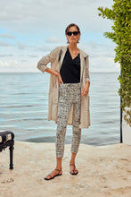 Load image into Gallery viewer, A stylish woman in a black top and white pants stands on a patio, showcasing captivating abstract print pull-on pants with side pockets.
