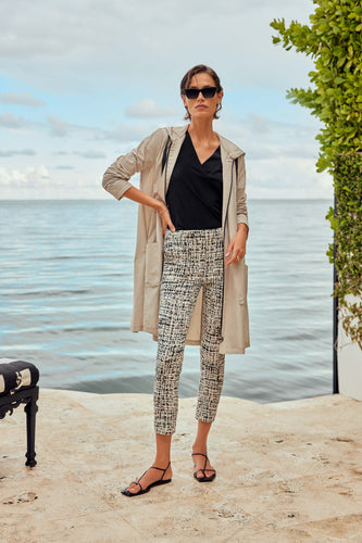 A stylish woman in a black top and white pants stands on a patio, showcasing captivating abstract print pull-on pants with side pockets.