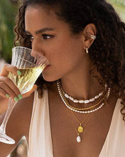 Load image into Gallery viewer, A woman in a white dress and pearls sips from a glass. She wears a charming pearl pendant necklace with a 1.5 cm long natural baroque pearl on a dainty gold block chain. 
