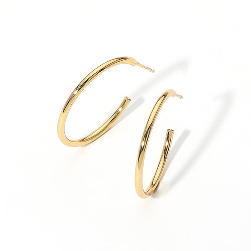 Gold hoop earrings set against a plain white background, casting soft shadows. The hoops are glossy, creating a sense of elegance and simplicity.