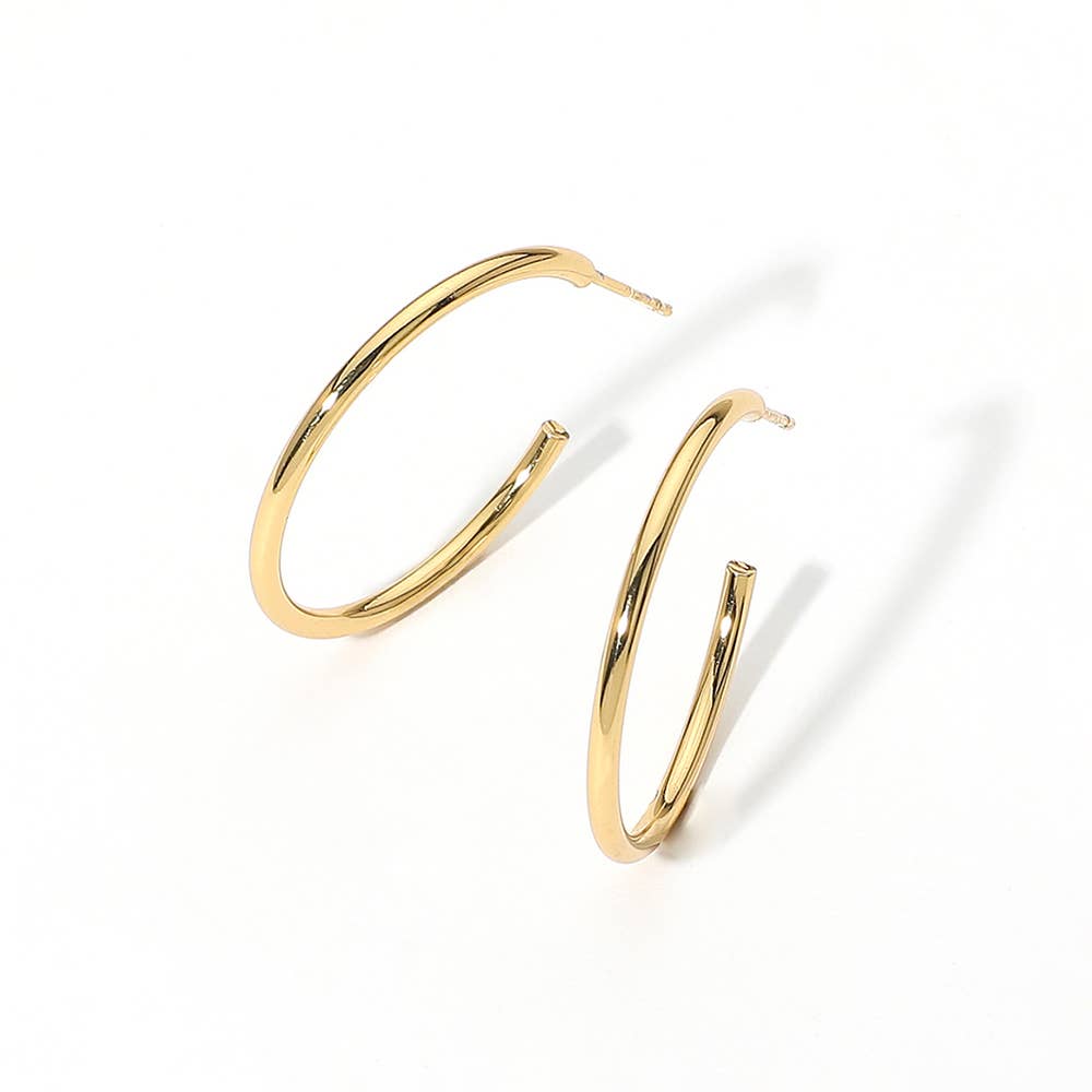 Gold hoop earrings set against a plain white background, casting soft shadows. The hoops are glossy, creating a sense of elegance and simplicity.