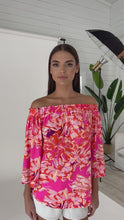 Load and play video in Gallery viewer, Julian Chang&#39;s Andrea Top Island Print: a vibrant island print top with a pink and orange color palette and bell sleeves, perfect for adding a playful touch to your outfit.

