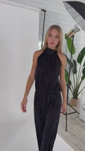 Load and play video in Gallery viewer, Black plisse Holly Jumpsuit by Julian Chang: Two-piece illusion jumpsuit with high mock neck, halter style straps, sleeveless bodice, and long straight leg pant.
