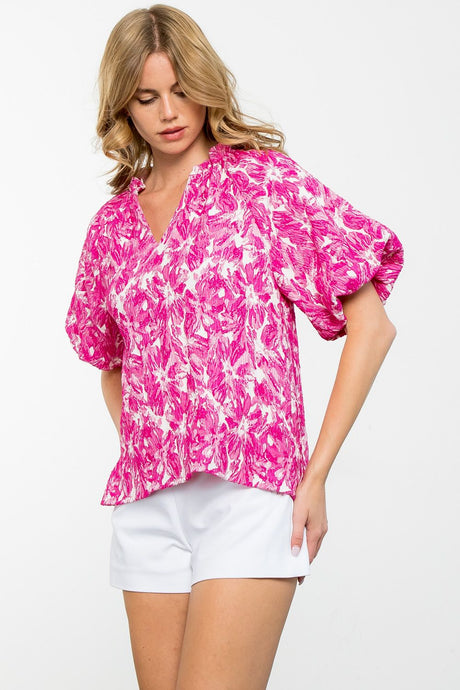 Get ready for spring with Dee, our Textured Flower Puff Sleeve Top by THML! This image shows a model wearing a pink floral top and white shorts, highlighting the pretty puff sleeves and unique flower design of the top.