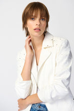 Load image into Gallery viewer, An elegant woman wearing a white jacket and jeans, featuring a stunning foiled suede jacket adorned with a guipure floral appliqué and statement studs.
