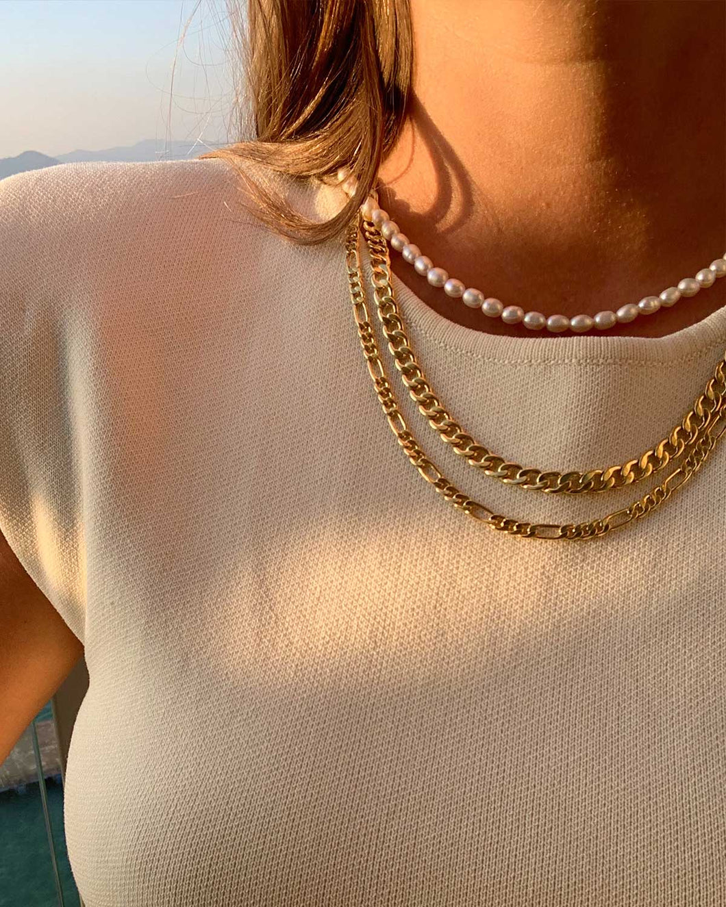 An elegant woman donning a white top and a gold chain necklace adorned with genuine freshwater pearls, adjustable in length.