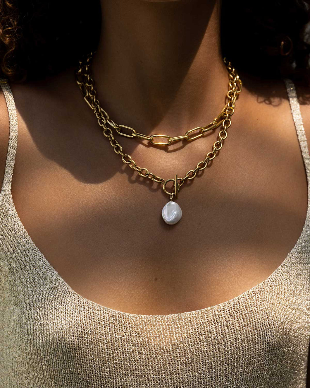 Enhance your style effortlessly with this pearl and gold chain necklace. Featuring a genuine freshwater pearl on a chunky gold chain, this necklace adds a touch of elegance to any outfit. The T bar closure and unique shape of the pearl make it a fashion-forward choice. Chain length: 45 cm.