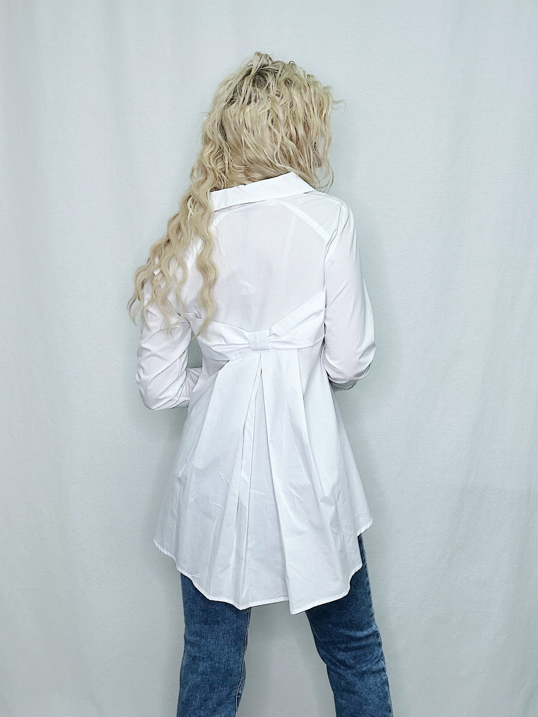 A white button-down blouse featuring a bow detail on the back, crafted from 100% cotton for a stylish look.